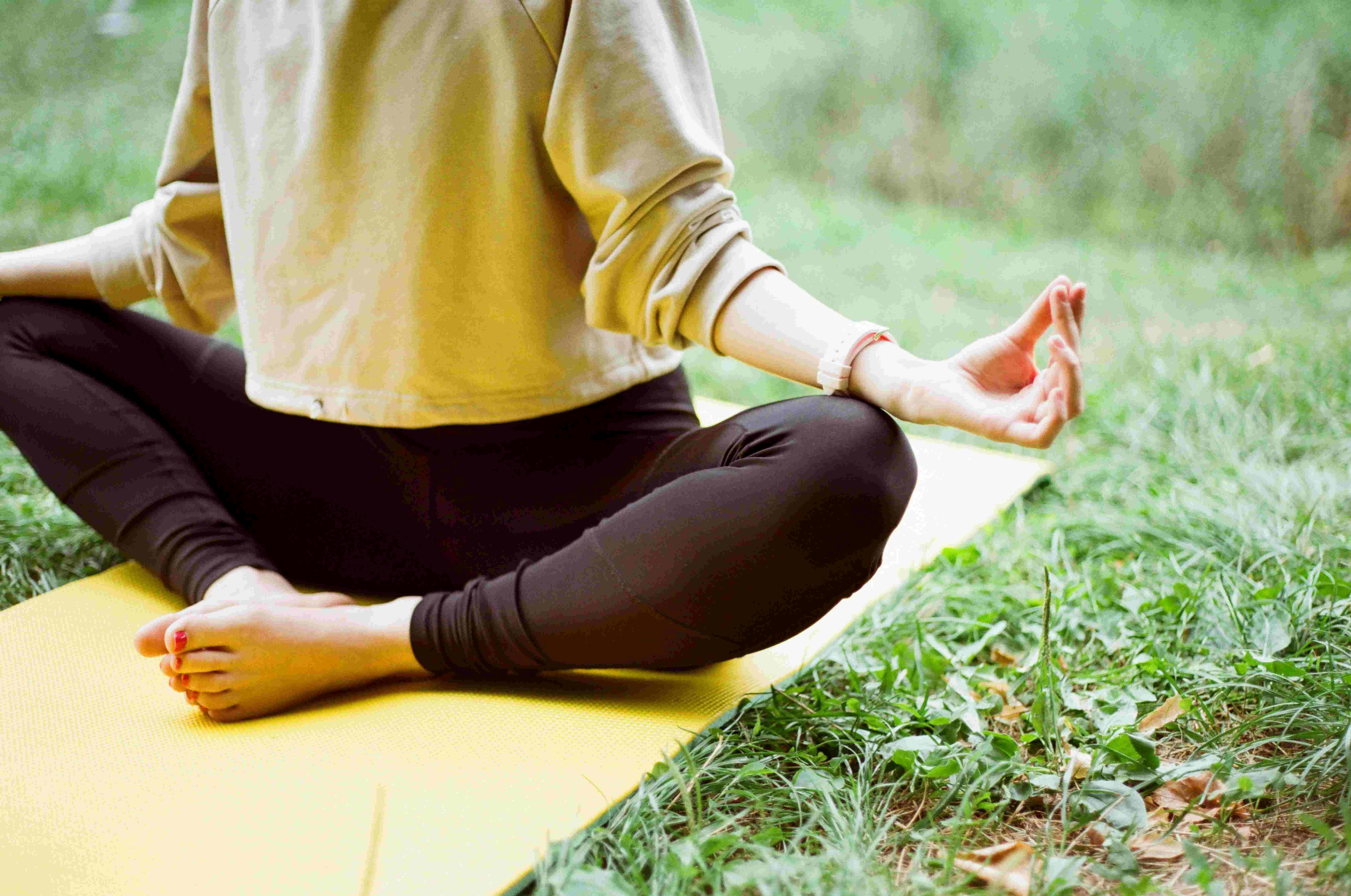 Žena meditující na yoga podložce na trávníku.